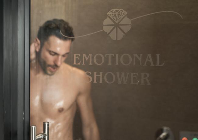 Man in emotional shower behind glass with writing.
