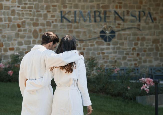 Paar in weißen Bademänteln geht zu einem Spa.