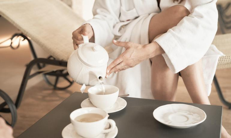 Woman pouring tea into cups, wearing a bathrobe, relaxing environment.