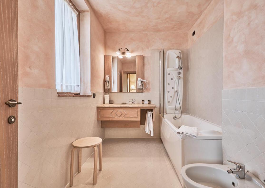 Bagno elegante con vasca, bidet e lavabo in legno, illuminato naturalmente.