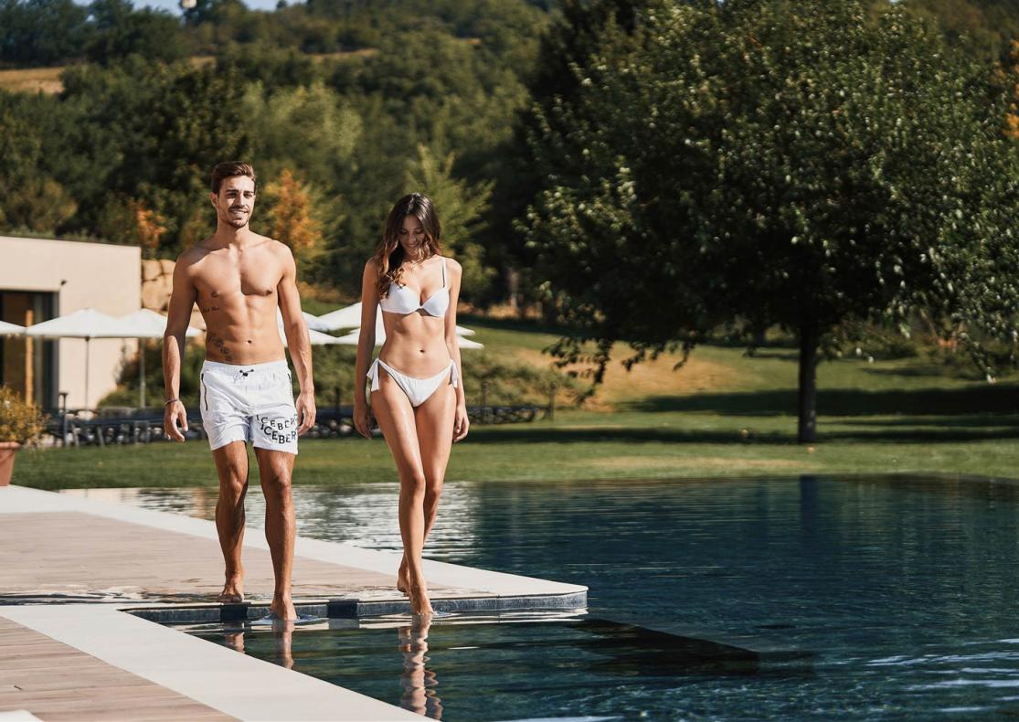 Zwei Personen gehen an einem Pool in einer natürlichen Umgebung spazieren.