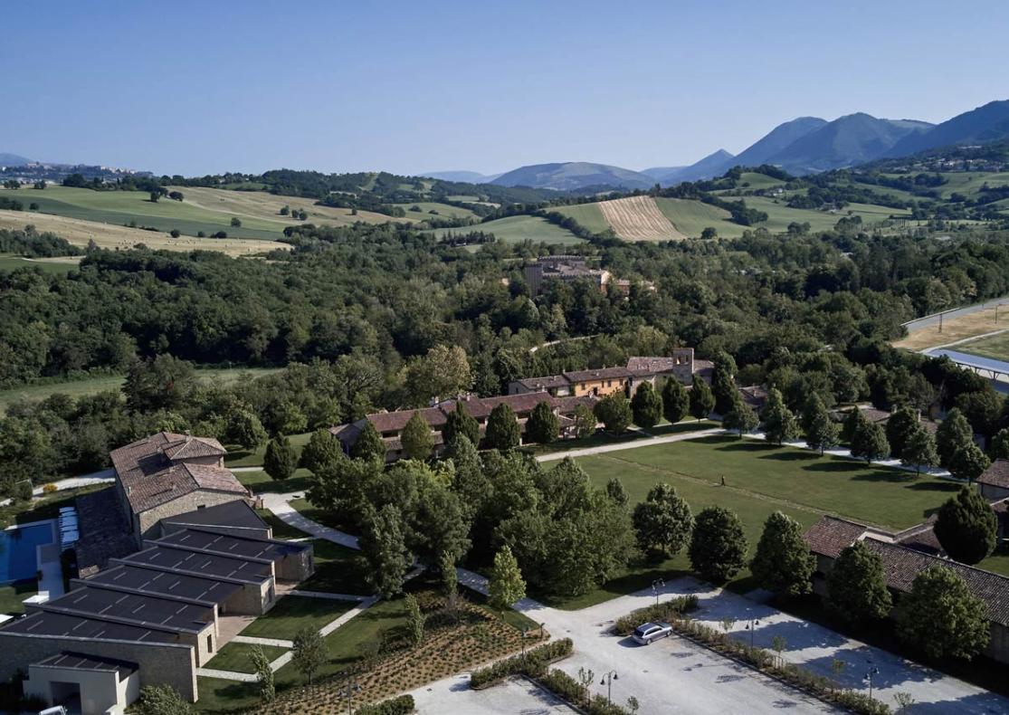 Ländliche Landschaft mit Feldern, Hügeln und einem Gebäudekomplex im Grünen.