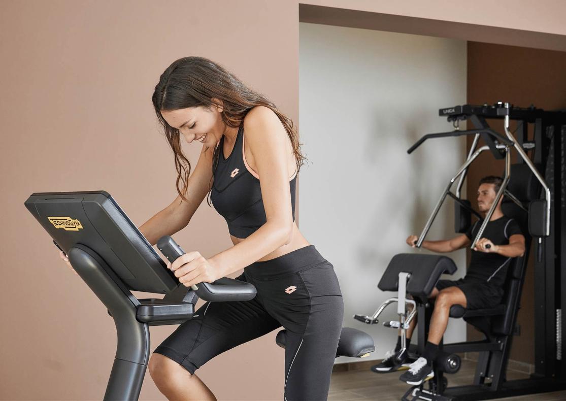 Due persone fanno esercizio in palestra con attrezzi moderni.
