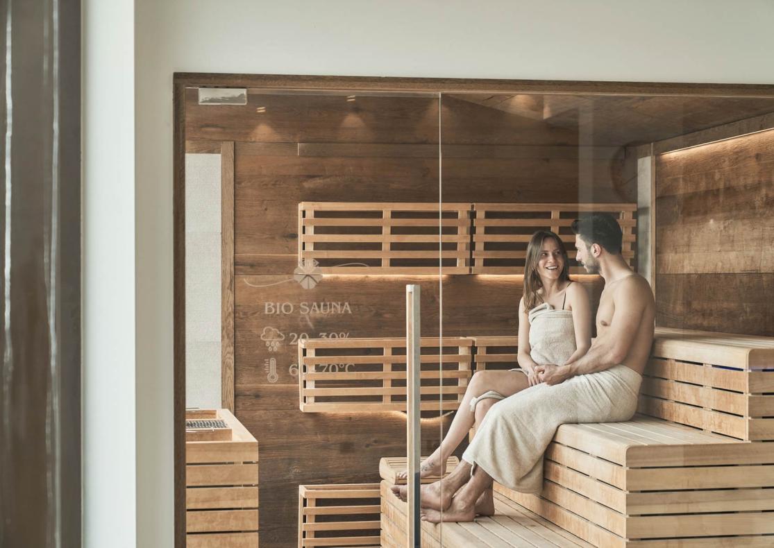 Due persone rilassano in una bio sauna con legno e luci soffuse.