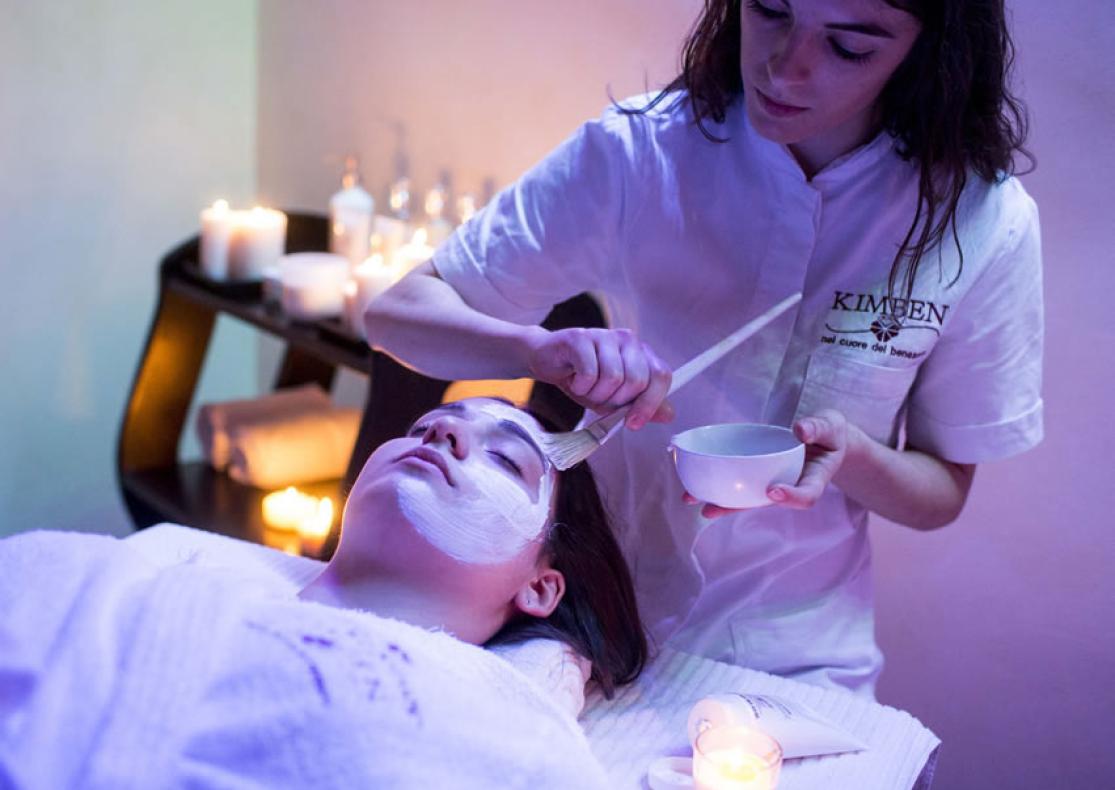Trattamento viso rilassante con maschera in una spa illuminata da candele.